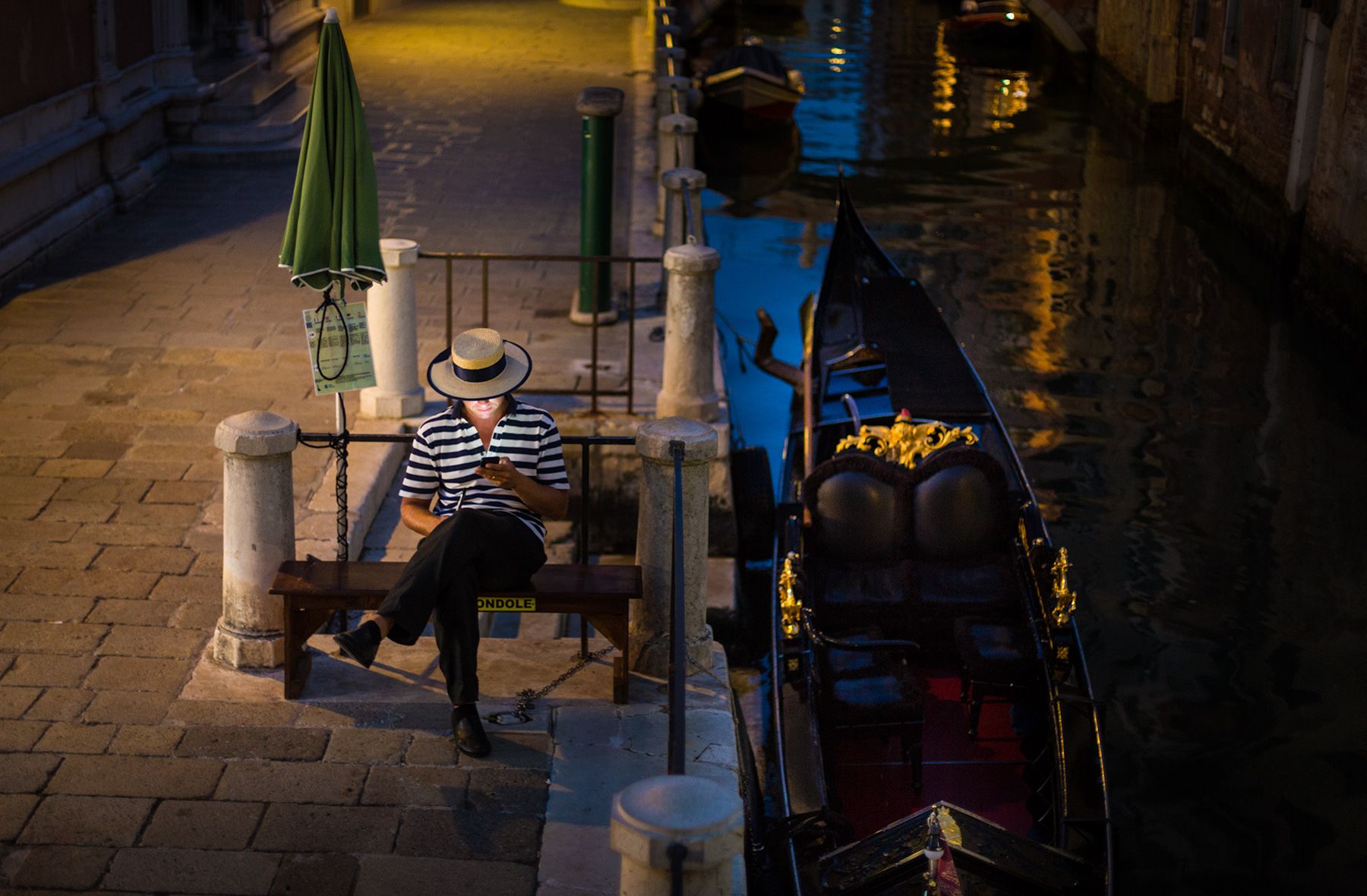 Venetian gondoliere at the end of his shift looking at his mobile phone with screen illuminating his face