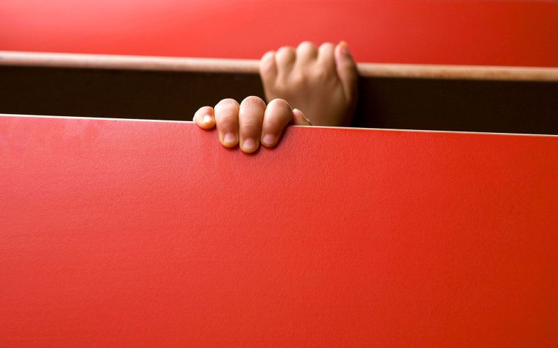 Shy boy hands behind a red bench in a diner, Albuquerque, New Mexico